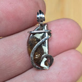 Silver pendant with a brown stone held between fingers against a blurred background