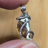 Silver pendant held between two fingers against a blurred background