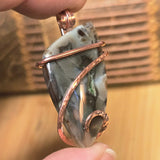Pendant with a stone and copper wire wrapping held by a hand against a blurred background