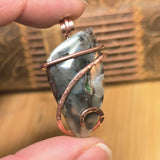 Hand holding a copper-wrapped stone pendant against a wooden background