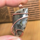 Pendant with stone and copper wire wrapping held between fingers against a textured background