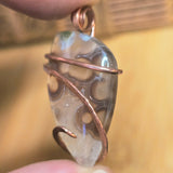 Hand holding a copper-wrapped crystal pendant against a blurred background