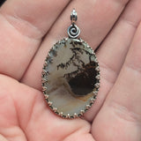 Oval-shaped pendant with a natural stone design held between fingers