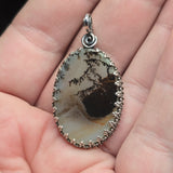 Oval-shaped pendant with natural stone design held in a hand