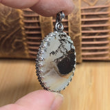 Oval-shaped pendant with intricate design held by a hand against a wooden background
