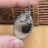 Close-up of a pendant with a natural stone design held between fingers on a wooden surface.