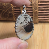 Close-up of a pendant with a natural stone design held between fingers on a wooden surface.