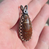 Dinosaur bone stone pendant with silver wire wrapping held in a hand