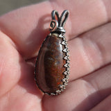 Dinosaur bone pendant with silver setting held between fingers