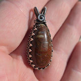 Dinobone stone pendant with silver setting held between fingers