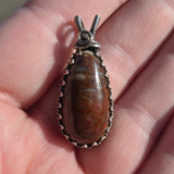 Close-up of a dinosaur stone pendant with silver setting held between fingers.