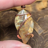 Plume agate pendant with copper wire wrapping held between fingers against a textured background