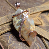Plume Agate pendant with copper wire on a textured metal surface