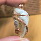 Moss agate pendant with copper wire wrapping held between fingers against a blurred background