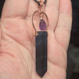 Dark fluorite pendant with a purple gemstone on a hand