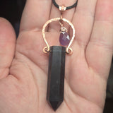Dark fluorite crystal pendant with gold and purple accents held in a hand.