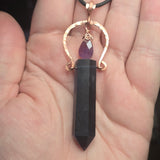 Dark fluorite crystal pendant with amethyst drop charm on a hand