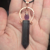 Dark fluorite crystal pendant with a purple gemstone on a hand