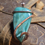 Green stone pendant with copper wire wrapping on a textured surface
