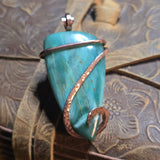 Green stone pendant with copper wire wrapping on a textured surface