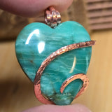 Turquoise green heart-shaped pendant with copper accents held between fingers against a blurred background