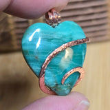 Turquoise green Jasper heart-shaped pendant with copper accents held between fingers against a blurred background