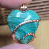 Turquoise green Jasper heart-shaped pendant with copper accents held between fingers