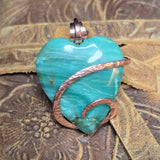 Green Jasper heart-shaped pendant with copper wire wrapping on a textured surface