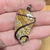 Hand holding a pendant with a textured stone design and copper wire wrapping.