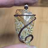 Pendant with natural stone design held between fingers against a wooden background