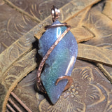Purple and green stone pendant with copper wire wrapping on a textured surface