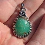 Green stone pendant with silver spiral design held between fingers