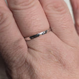 A simple, sleek sterling silver band ring with a hammered finish, displayed on a person's hand.