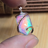 Multicolored opal pendant held between fingers on a wooden surface