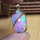 Opal pendant with gold wire wrapping held between fingers on a wooden surface