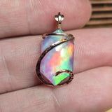 Opal pendant with gold wire wrapping held between fingers