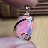 Opal pendant held between fingers with a blurred background
