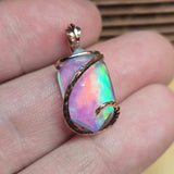 Multicolored opal pendant with rose gold setting held between fingers