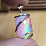 Multicolored opal pendant held between fingers with a blurred background