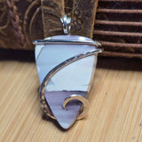 Jewelry pendant with light pastel stone and gold accents on a wooden surface