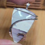 Close-up of a pendant with a pastel stone and gold and silver wire wrapping on a wooden surface.