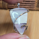 Silver-wrapped stone pendant held between fingers against a wooden background