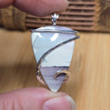 Hand holding a light pastel stone pendant with silver and gold accents on a wooden surface
