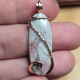 Marble-patterned pendant with rose gold wire wrapping held between fingers.