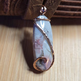 Decorative pendant with a textured stone and rose gold wire wrapping on a wooden surface
