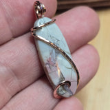 Hyacinth Jasper stone pendant with rose gold wire wrapping held between fingers
