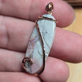Marble-patterned pendant with rose gold accents held between fingers