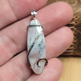 White marbled stone pendant with silver wire wrapping held in a hand.