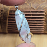 Marble stone pendant with silver wire wrapping held by a hand against a blurred background