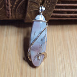 Pink stone pendant with silver wire on a brown textured surface